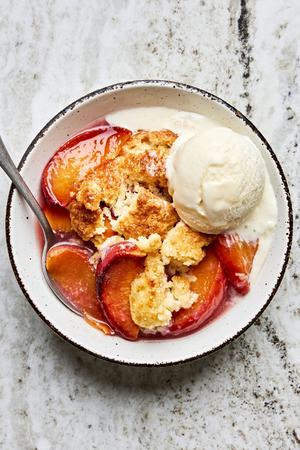 a bowl of peach cobbler made with homemade biscuits and topped with vanilla ice cream