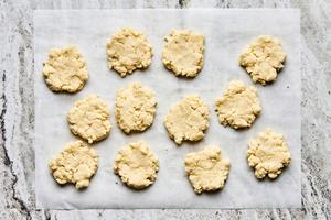 raw biscuit dough formed into patty shapes on parchment paper on the counter
