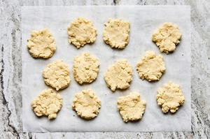 raw biscuit dough formed into patty shapes on parchment paper on the counter