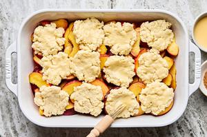 a baking dish of seasoned peaches topped with biscuit dough being brushed with egg wash
