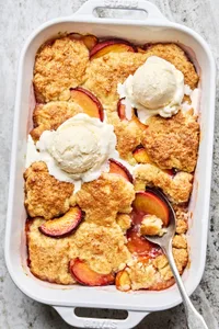 homemade peach cobbler in a baking dish topped with two scoops of vanilla ice cream