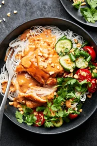 a peanut chicken noodle bowl made with rice noodles topped with chicken, peanut sauce, green bean & tomato salad & cilantro