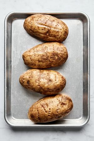 4 baked potatoes on a rimmed baking sheet