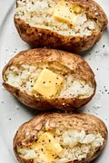 perfect baked potatoes cut open and topped with butter, salt and pepper