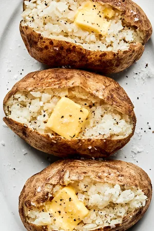 perfect baked potatoes cut open and topped with butter, salt and pepper