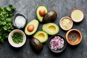 avocados, garlic, pepper, cilantro, jalapeño, red onion, limes and salt in prep bowls to make guacamole
