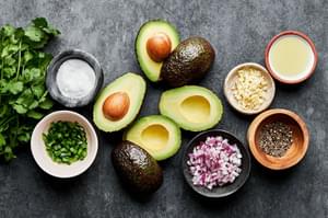 avocados, garlic, pepper, cilantro, jalapeño, red onion, limes and salt in prep bowls to make guacamole