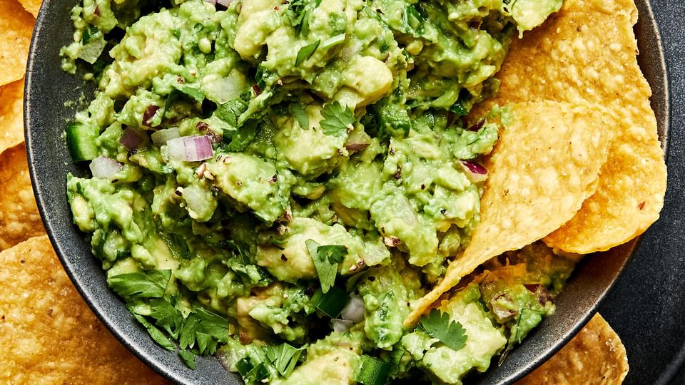 a bowl of homemade guacamole with red onion, jalapeño and cilantro surrounded by tortilla chips