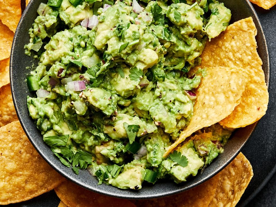 a bowl of homemade guacamole with red onion, jalapeño and cilantro surrounded by tortilla chips