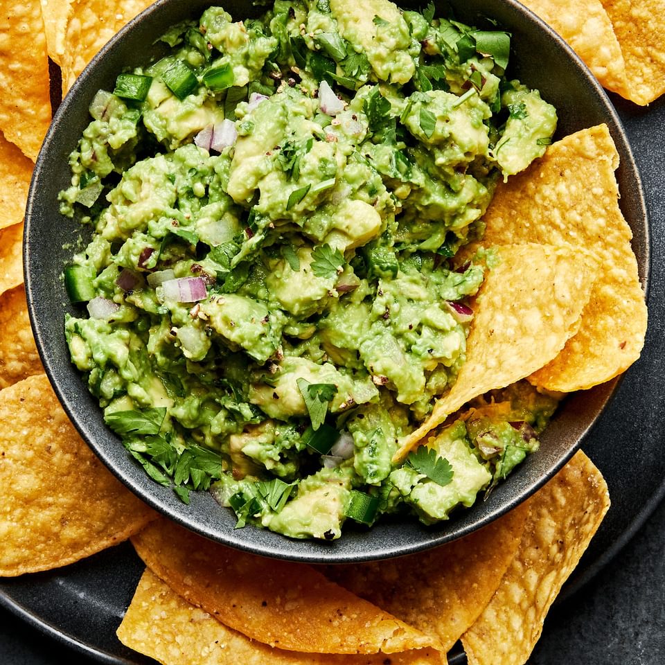 a bowl of homemade guacamole with red onion, jalapeño and cilantro surrounded by tortilla chips
