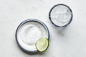 a salt rimmed glass filled with ice next to a bowl of salt
