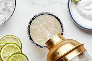 a margarita being poured out of a cocktail shaker into an ice-filled glass with a salt rim