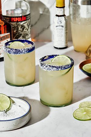 margaritas served in salt rimmed glasses with lime wedges surrounded by margarita ingredients