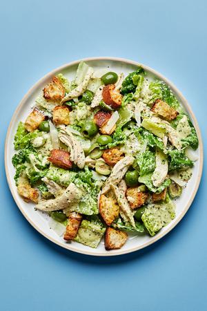 Pesto Caesar Salad with castelvetrano Olives, shredded chicken, parmesan and homemade croutons on a plate