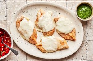 baked chicken with melted mozzarella on a serving platter next to bowl of bruschetta and pesto