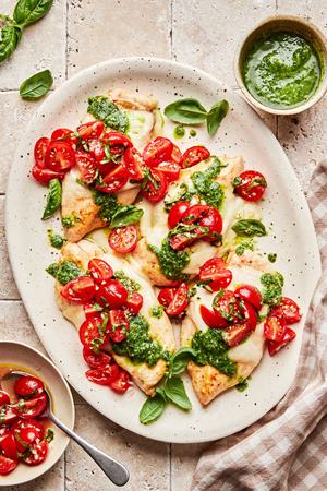 Pesto chicken bruschetta on a serving platter. Chicken topped with melted mozzarella, pesto and bruschetta.
