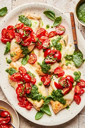Pesto chicken bruschetta on a serving platter. Chicken topped with melted mozzarella, pesto and bruschetta.