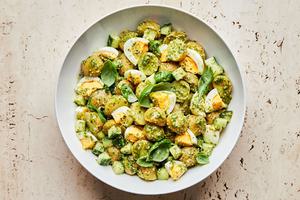pesto potato salad in a serving bowl made with potatoes, eggs, cucumbers and fresh basil