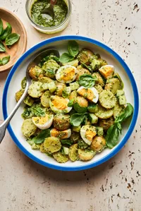 pesto potato salad in a serving bowl made with potatoes, eggs, cucumbers and fresh basil