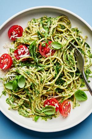 a plate of homemade pesto spaghetti with arugula and cherry tomatoes and sprinkled with basil and parmesan