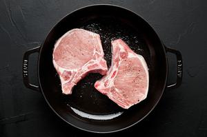 2 bone in pork chops seasoned with salt and pepper being browned in olive oil in a skillet