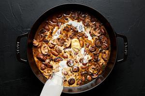 heavy cream being added to a skillet filled with butter sautéed mushrooms with white wine and thyme
