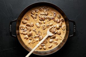 creamy mushroom sauce in a skillet, being stored with a wooden spoon
