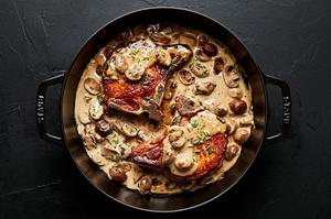 2 bone in pork chops in a skillet filled with creamy mushroom sauce