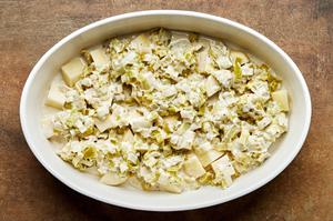 potatoes, leek cream sauce, cheese and chives being layered in a baking dish