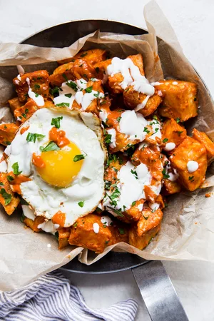 a dish of homemade patatas Bravas topped with garlic aioli, fresh parsley and a fried egg