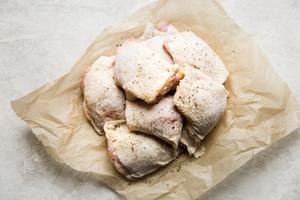 chicken thighs seasoned with salt and black pepper on parchment paper