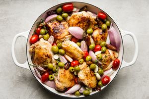 browned chicken thighs in a pan with olives, tomatoes and shallots.