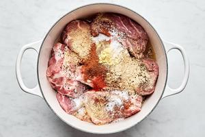 boneless pork shoulder, spices, apple cider vinegar and chicken stock being added to a pot