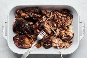 cooked pork shoulder being shredded into pulled pork with 2 forks
