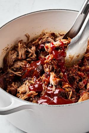 a pot of pulled pork made with boneless pork shoulder, spices, apple cider vinegar and chicken stock drizzled with bbq sauce