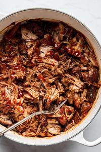a pot of pulled pork made with boneless pork shoulder, spices, apple cider vinegar and chicken stock drizzled with bbq sauce