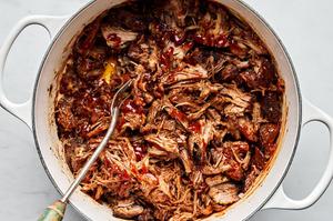 a pot of pulled pork made with boneless pork shoulder, spices, apple cider vinegar and chicken stock drizzled with bbq sauce