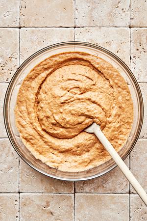 homemade pumpkin pancake batter being stirred in a glass bowl with a wooden spoon