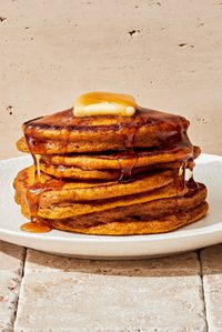 a stack of homemade pumpkin pancakes topped with a pat of butter and dripping with maple syrup, the perfect fall breakfast