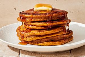 a stack of homemade pumpkin pancakes topped with a pat of butter and dripping with maple syrup