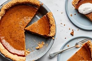 a homemade pumpkin pie being sliced onto plates and topped with whipping cream