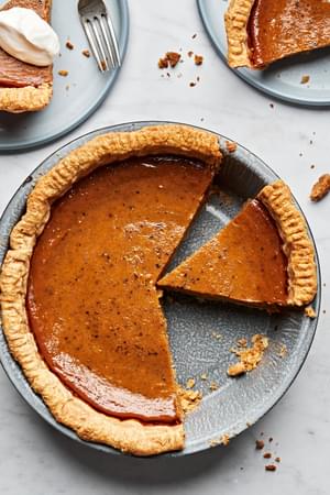 a homemade pumpkin pie being sliced onto plates and topped with whipping cream