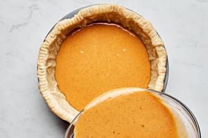 pumpkin pie filling being poured into a par-baked crust