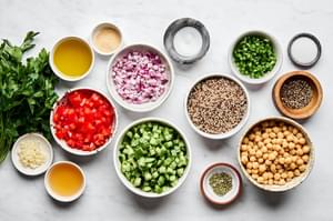 quinoa, basil, garlic, chick peas, red onion, cucumber, tomato, jalapeño and parsley in separate bowls to make quinoa salad