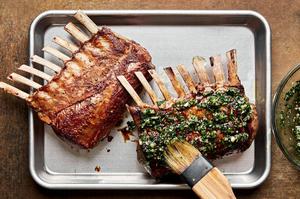 Roasted rack of lamb being brushed with mint sauce on a baking sheet
