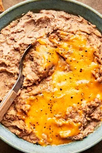 homemade refried beans topped with melted cheddar cheese in a bowl with a spoon