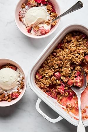 rhubarb crisp being spooned into serving bowls topped with vanilla ice cream