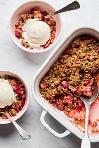 rhubarb crisp being spooned into serving bowls topped with vanilla ice cream