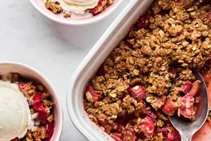 rhubarb crisp being spooned into serving bowls topped with vanilla ice cream