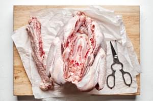 a raw turkey with the spine cut out on top of parchment paper